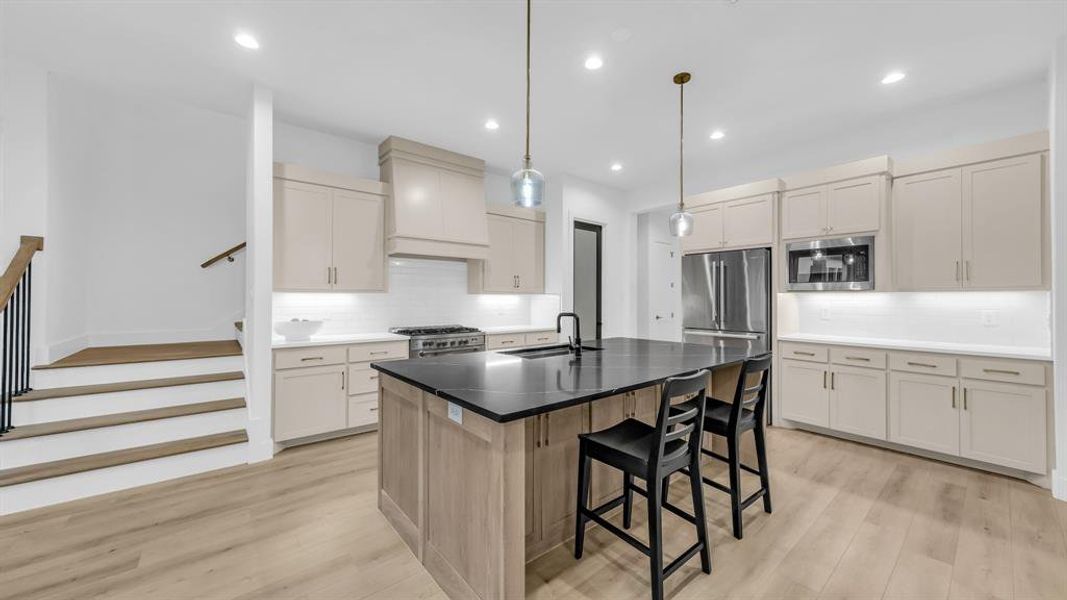 Kitchen with appliances with stainless steel finishes, a sink, premium range hood, decorative backsplash, and a kitchen breakfast bar Kitchen with appliances with stainless steel finishes, a sink, premium range hood, decorative backsplash, and a kitchen breakfast bar