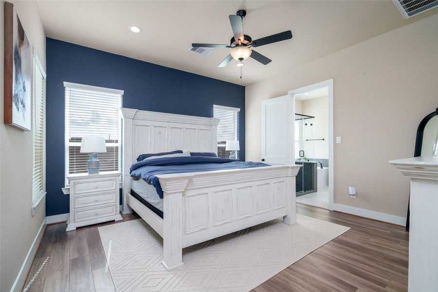 Retreat to the serene primary bedroom, featuring windows with privacy blinds, elegant vinyl plank flooring, custom accent wall, and a stylish ceiling fan for ultimate comfort and relaxation! Retreat to the serene primary bedroom, featuring windows with privacy blinds, elegant vinyl plank flooring, custom accent wall, and a stylish ceiling fan for ultimate comfort and relaxation!