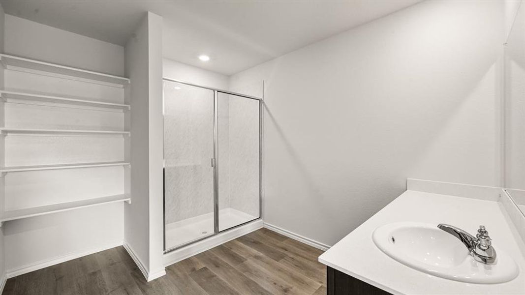 Bathroom featuring a glass-enclosed shower, built-in shelving, a single vanity with an integrated sink, polished chrome faucet, and wood-finish flooring Bathroom featuring a glass-enclosed shower, built-in shelving, a single vanity with an integrated sink, polished chrome faucet, and wood-finish flooring