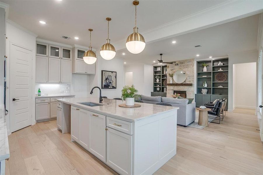 Kitchen featuring custom cabinetry to the ceiling, light hardwood floors, large island with Quartzite countertops opens to living area with built in cabinets and stone fireplace.