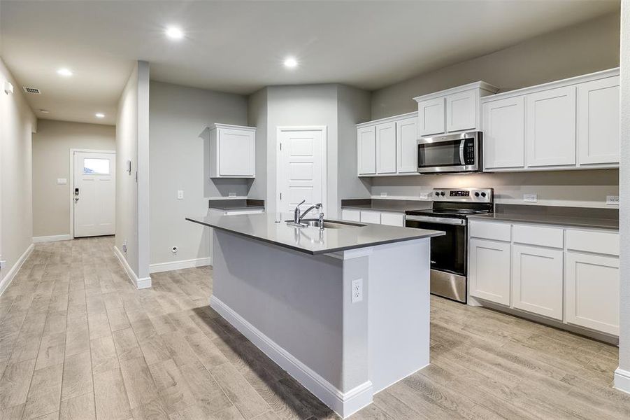 Kitchen featuring appliances with stainless steel finishes, recessed lighting, white cabinetry, light wood-style flooring, and a kitchen island with sink Kitchen featuring appliances with stainless steel finishes, recessed lighting, white cabinetry, light wood-style flooring, and a kitchen island with sink