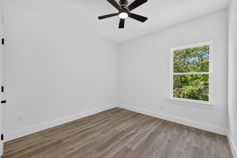 Spacious room featuring wood-finish flooring, crisp white walls, and a contemporary ceiling fan with integrated lighting Spacious room featuring wood-finish flooring, crisp white walls, and a contemporary ceiling fan with integrated lighting
