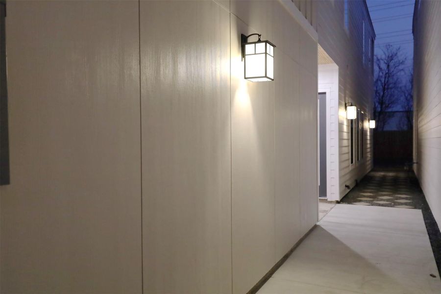 A pendant-lit concrete walkway welcomes you to the front entry, while the rear features gravel accented with diamond-laid pavers, combining elegance with low-maintenance design.