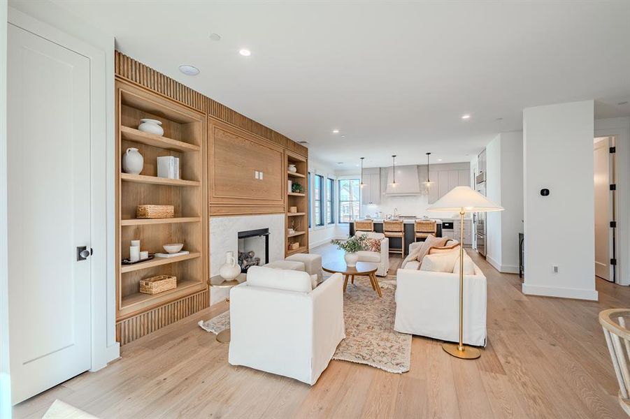 Living room featuring light wood-type flooring, recessed lighting, a fireplace, and built in features