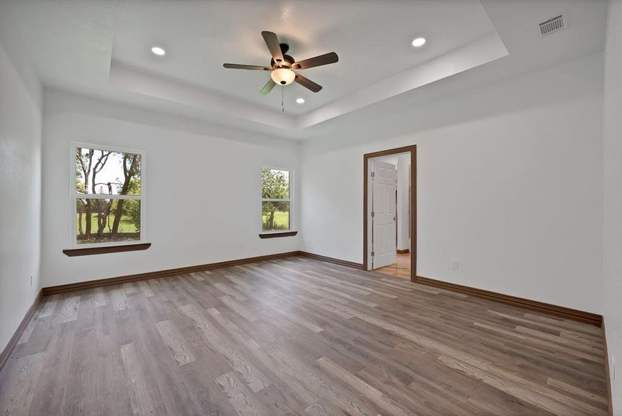 Empty room featuring a raised ceiling, light wood-style flooring, ceiling fan, and recessed lighting