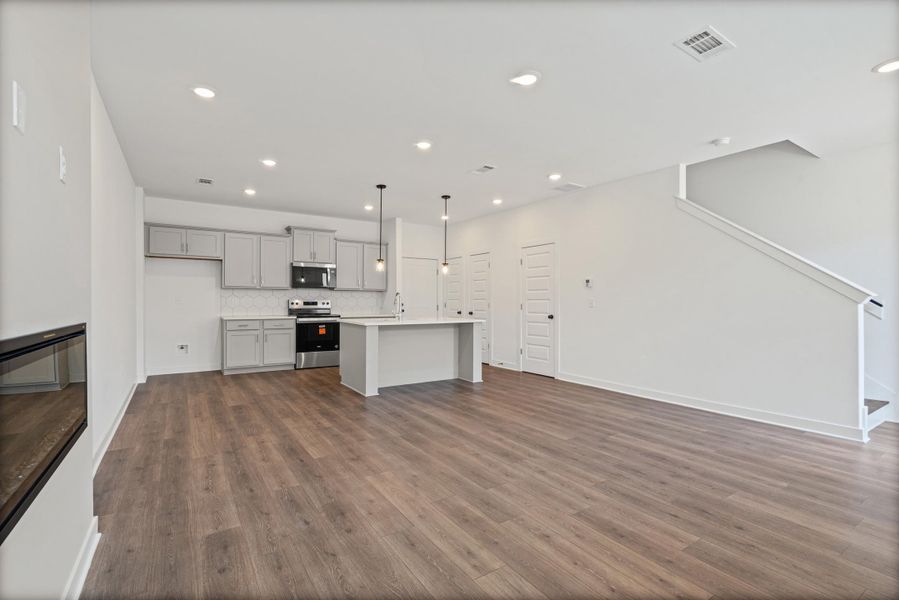 Open-concept living space featuring wood-finish flooring, a built-in electric fireplace, recessed lighting, and a kitchen with gray cabinetry, white countertops, and stainless steel appliances