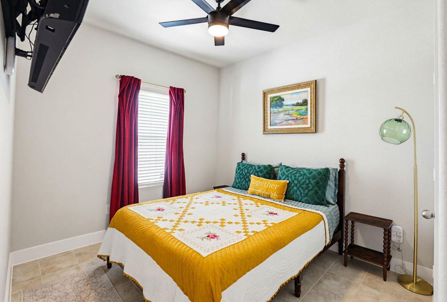 Bedroom featuring tile flooring, a window with horizontal blinds and red drapery, and a ceiling fan with integrated lighting