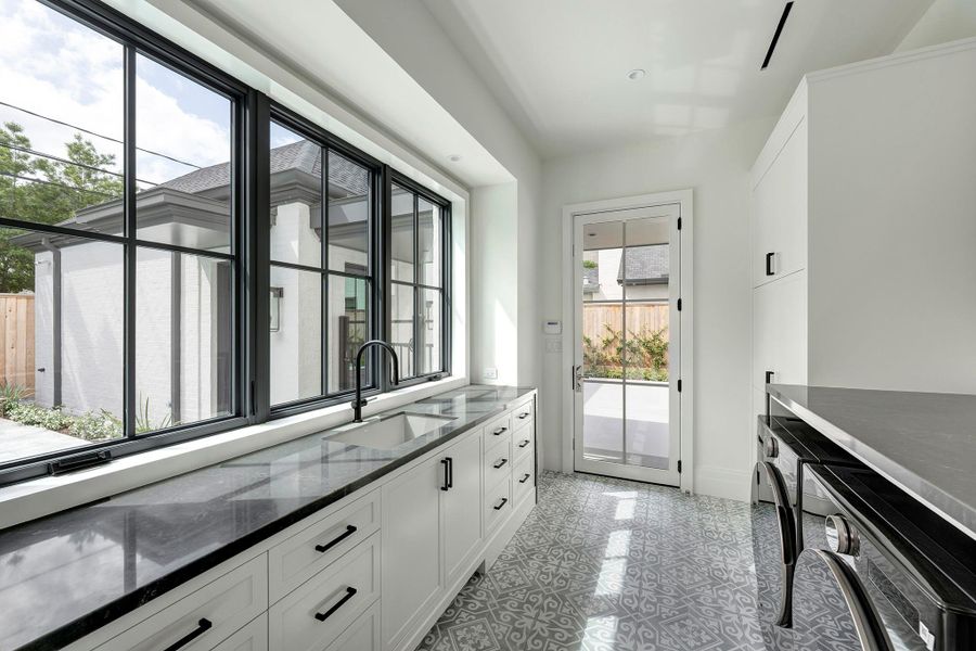 Utility room is sleek and functional with sink, quartz counters and abundant cabinetry.
