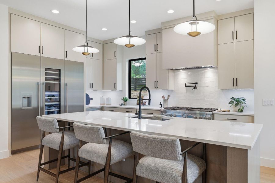 Contemporary kitchen featuring a large central island, light wood-finish flooring, full-height cabinetry with dark hardware, stainless steel appliances, and a tiled backsplash
