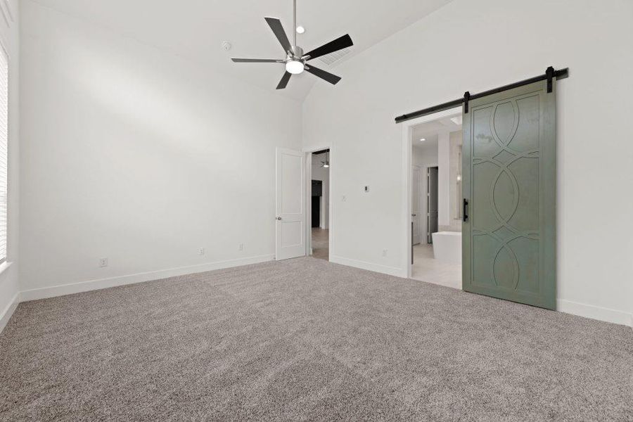 A spacious primary bedroom with soaring vaulted ceilings, plush carpeting, and a stylish barn door leading to the ensuite bathroom.