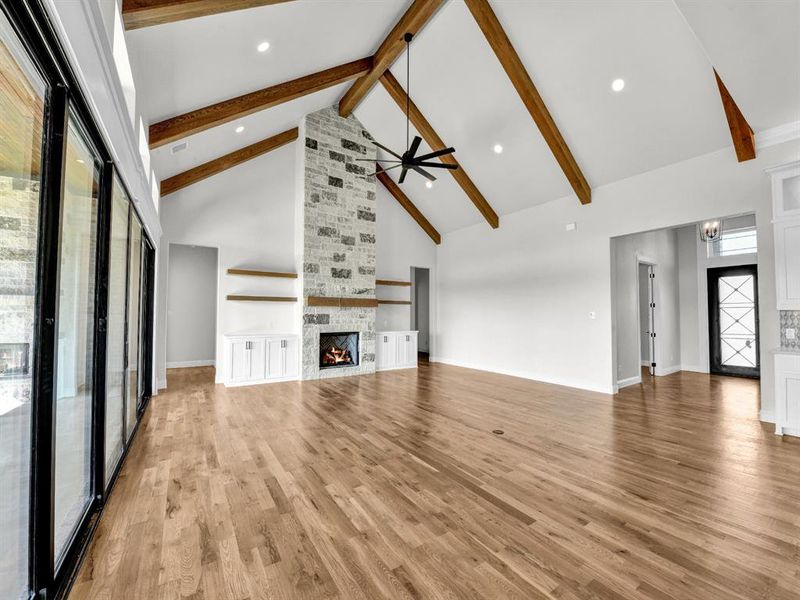 Unfurnished living room featuring high vaulted ceiling, beamed ceiling, light wood-type flooring, and a stone fireplace