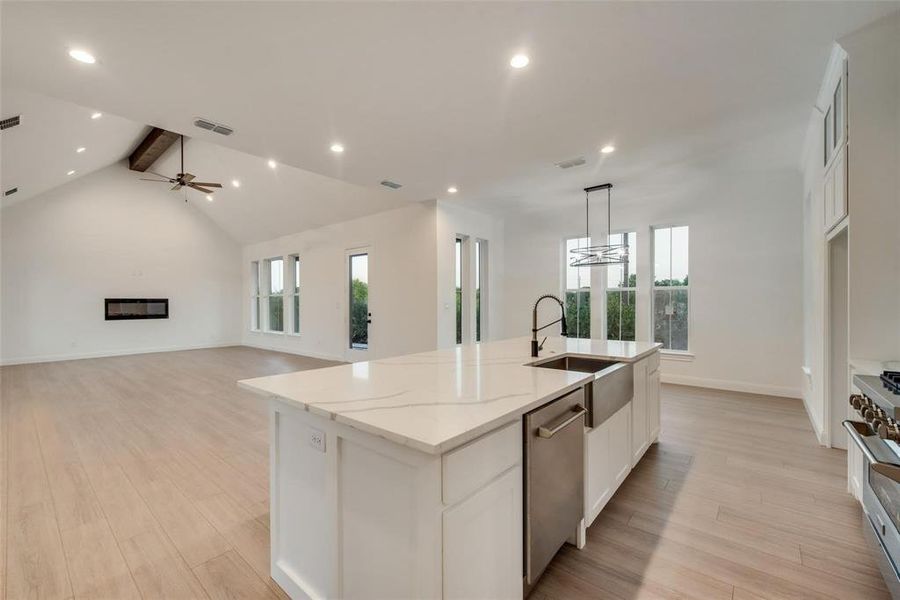 Kitchen featuring beam ceiling, white cabinets, light stone counters, light wood finished floors, and a kitchen island with sink