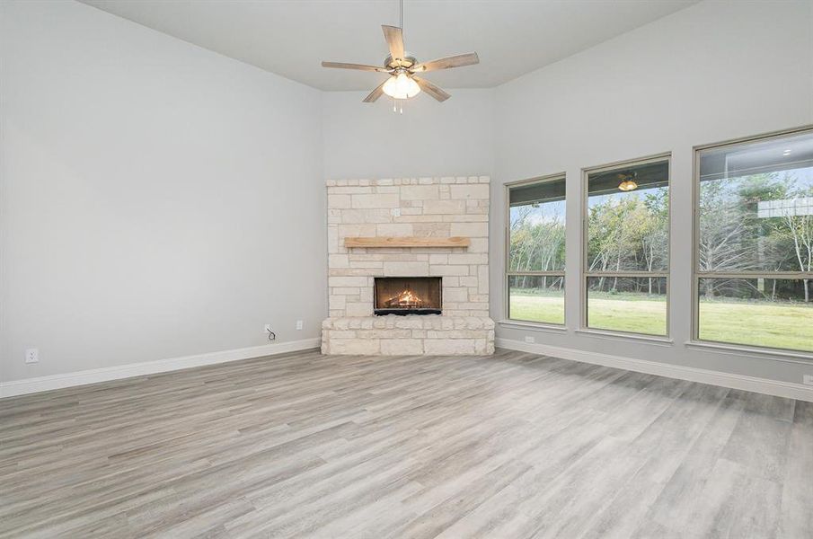 Unfurnished living room featuring ceiling fan, light hardwood / wood-style floors, and a stone fireplace