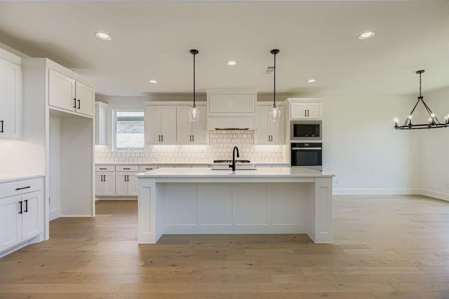 Kitchen featuring decorative light fixtures, white cabinetry, a kitchen island with sink, recessed lighting, and light wood-style flooring