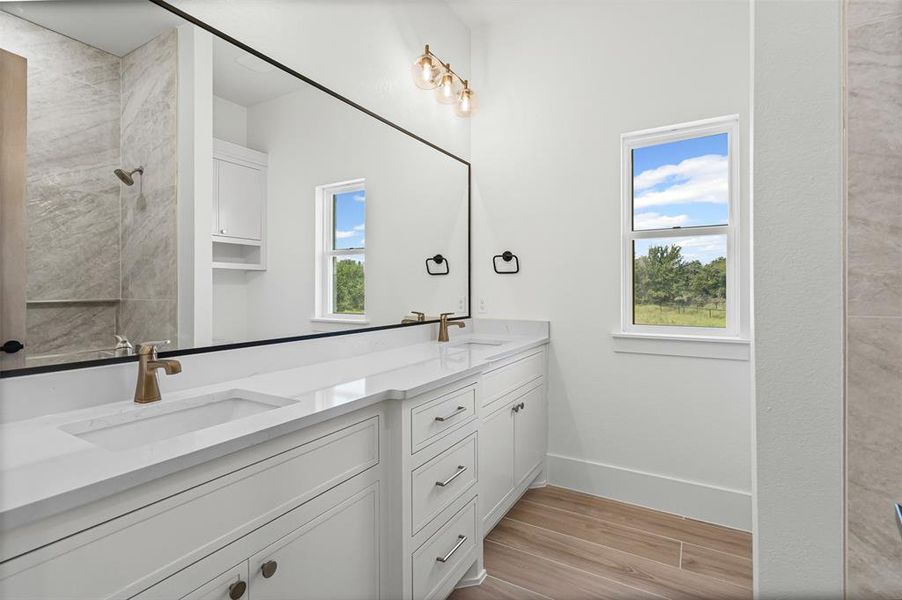 Bathroom with double vanity, light wood finished floors, and a tile shower Bathroom with double vanity, light wood finished floors, and a tile shower