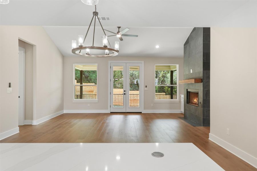 Unfurnished living room featuring wood finished floors, a chandelier, a fireplace, baseboards, and lofted ceiling Unfurnished living room featuring wood finished floors, a chandelier, a fireplace, baseboards, and lofted ceiling