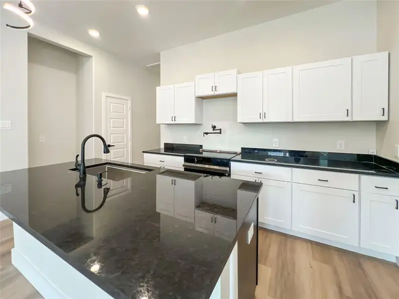 Kitchen with a sink, light wood-style floors, dark stone counters, a center island with sink, and white cabinetry