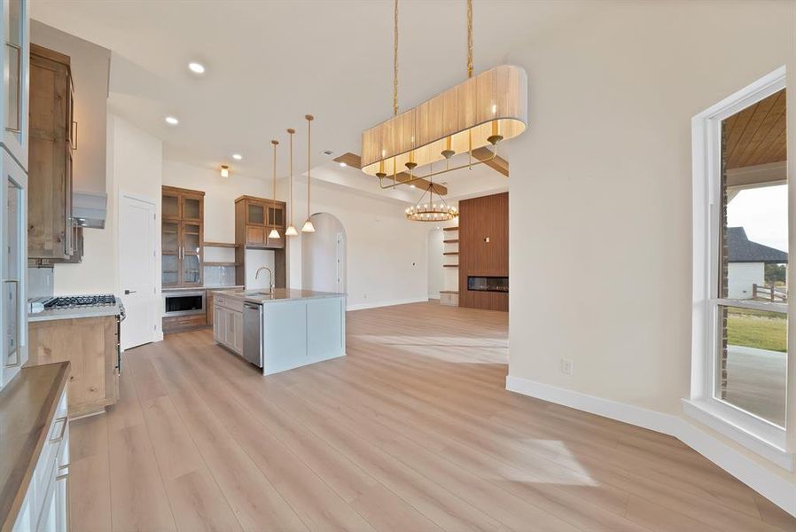Kitchen with open floor plan, glass insert cabinets, arched walkways, pendant lighting, and an island with sink Kitchen with open floor plan, glass insert cabinets, arched walkways, pendant lighting, and an island with sink