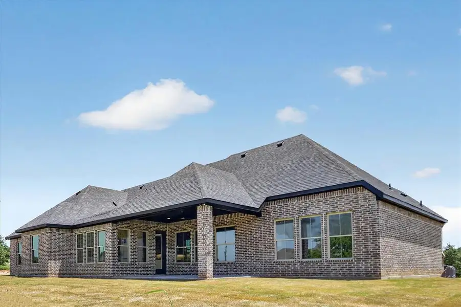 Brick exterior featuring a covered patio, multiple windows, and a shingled roof