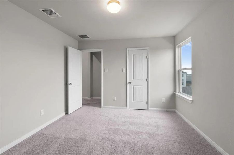 A quiet bedroom offers plush carpeting, a wide window, and multiple entryways for comfort and ease.