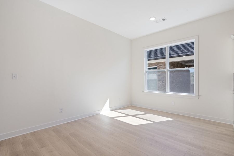 Neutral interior space featuring wood-finish flooring, crisp white walls, and a large window with white trim, accented by a recessed ceiling light Neutral interior space featuring wood-finish flooring, crisp white walls, and a large window with white trim, accented by a recessed ceiling light