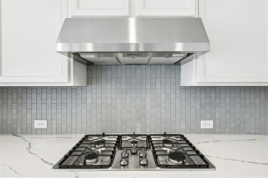 Kitchen view of stainless steel gas stovetop, light stone counters, and white cabinetry