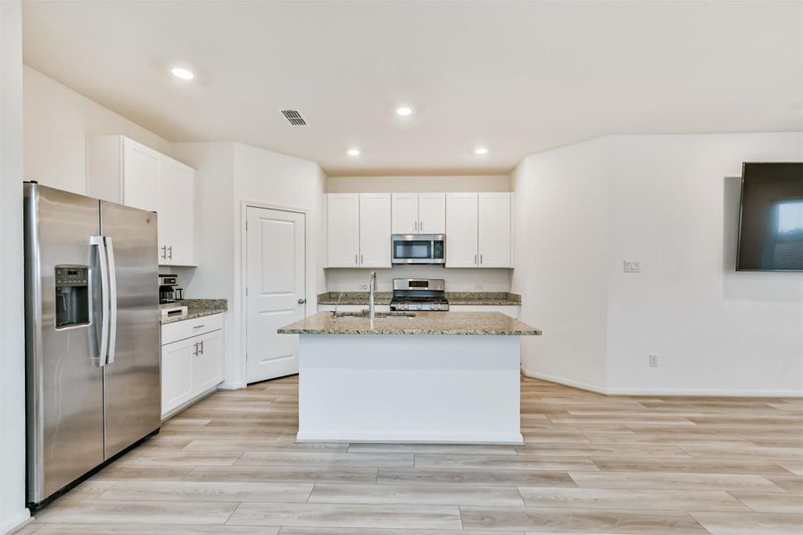 This modern kitchen features sleek stainless steel appliances included a convection oven that also acts as an air fryer, white cabinetry, granite countertops, and a central island. The open layout and recessed lighting create a bright, inviting space.