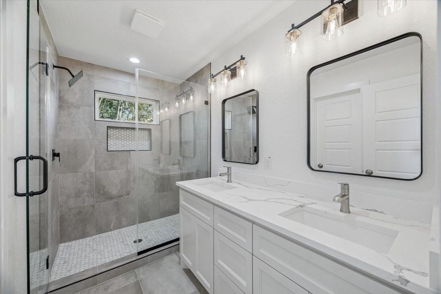 Primary bedroom en suite with double sinks, frameless shower doors, and ample lighting.
