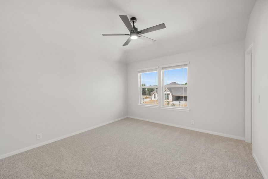 Empty bedroom with vaulted ceiling, ceiling fan, carpet flooring, and double windows overlooking neighborhood homes Empty bedroom with vaulted ceiling, ceiling fan, carpet flooring, and double windows overlooking neighborhood homes