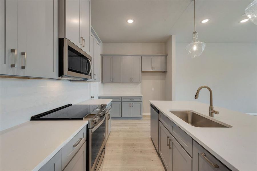 Kitchen with light hardwood / wood-style flooring, stainless steel appliances, gray cabinetry, tasteful backsplash, and sink