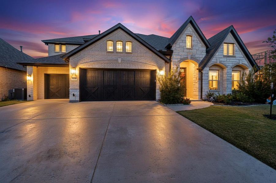 French country style house with brick siding, concrete driveway, stone siding, a front lawn, and an attached garage French country style house with brick siding, concrete driveway, stone siding, a front lawn, and an attached garage
