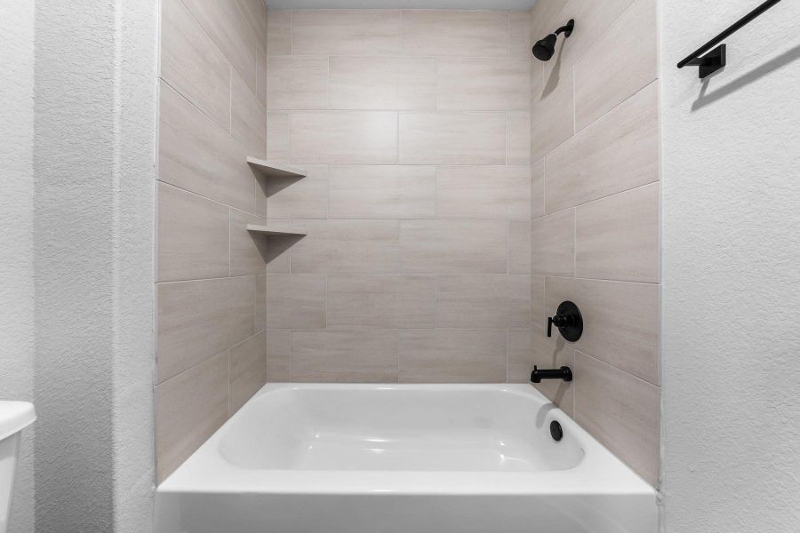 Bathroom with a textured wall and shower / washtub combination