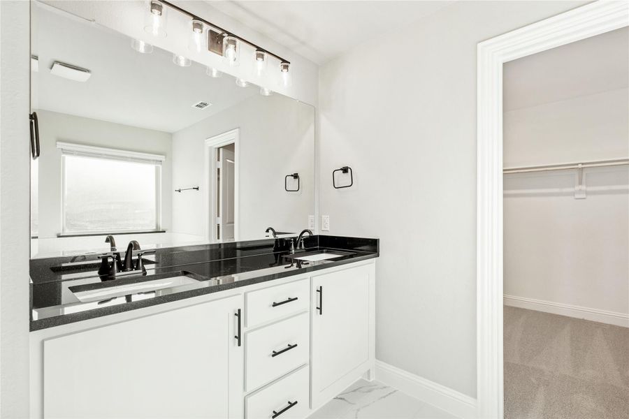 Bathroom with double sink vanity, white cabinets, dark countertop, and walk-in closet entrance Bathroom with double sink vanity, white cabinets, dark countertop, and walk-in closet entrance