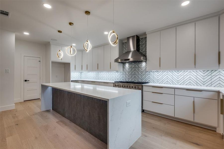 Kitchen featuring white cabinets, wall chimney exhaust hood, hanging light fixtures, modern cabinets, and tiled backsplash