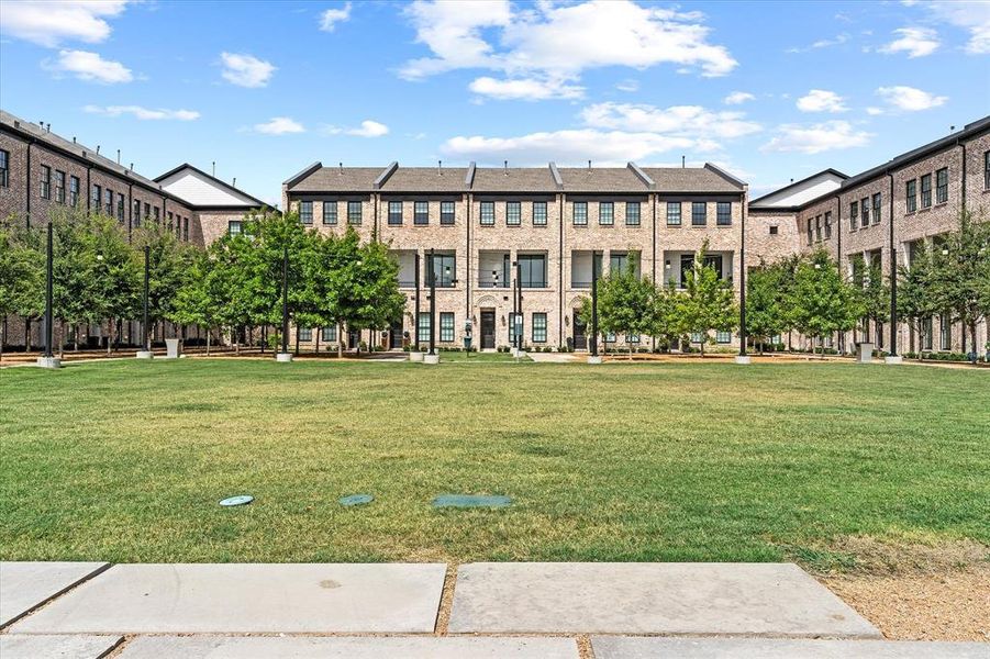 Community green space with a manicured lawn, framed by modern townhomes featuring brick facades, dark-framed windows, and private balconies