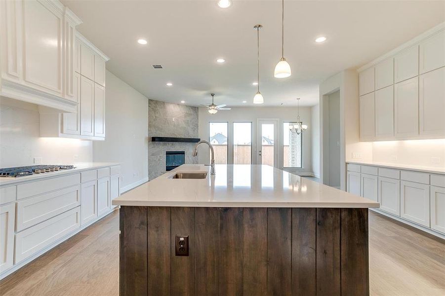 Kitchen with a center island with sink, sink, a stone fireplace, and light wood-type flooring