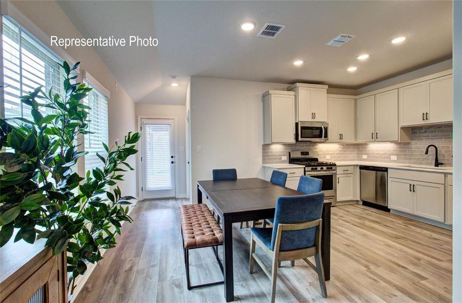 Open-concept kitchen and dining area featuring light wood-finish flooring, recessed lighting, and a white subway tile backsplash