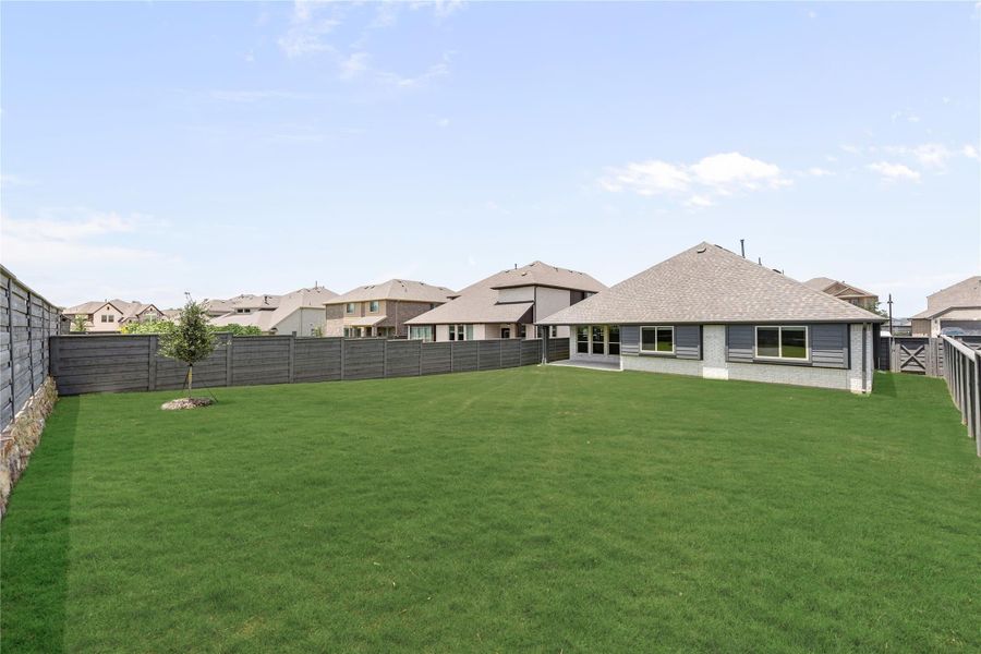 Large backyard with green lawn, wood privacy fence, and single-story brick home with covered patio Large backyard with green lawn, wood privacy fence, and single-story brick home with covered patio