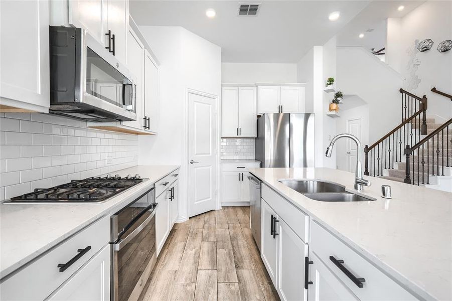 Kitchen with light stone countertops, stainless steel appliances, white cabinets, light wood-style floors, and backsplash Kitchen with light stone countertops, stainless steel appliances, white cabinets, light wood-style floors, and backsplash