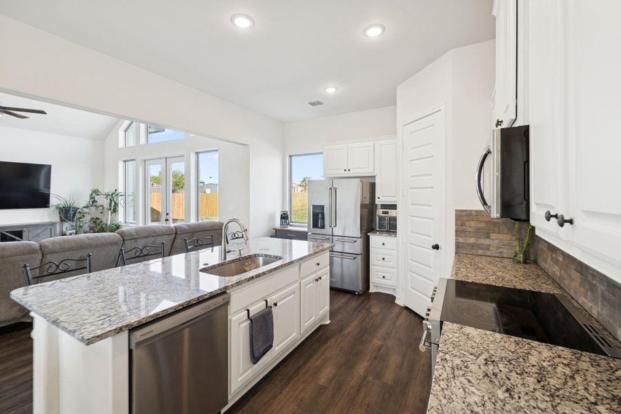 Kitchen featuring dark wood finished floors, appliances with stainless steel finishes, light stone countertops, a kitchen island with sink, and open floor plan Kitchen featuring dark wood finished floors, appliances with stainless steel finishes, light stone countertops, a kitchen island with sink, and open floor plan