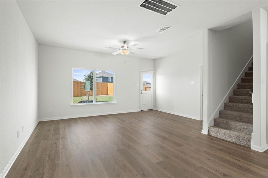 Unfurnished living room featuring dark wood-style floors, ceiling fan, and stairs