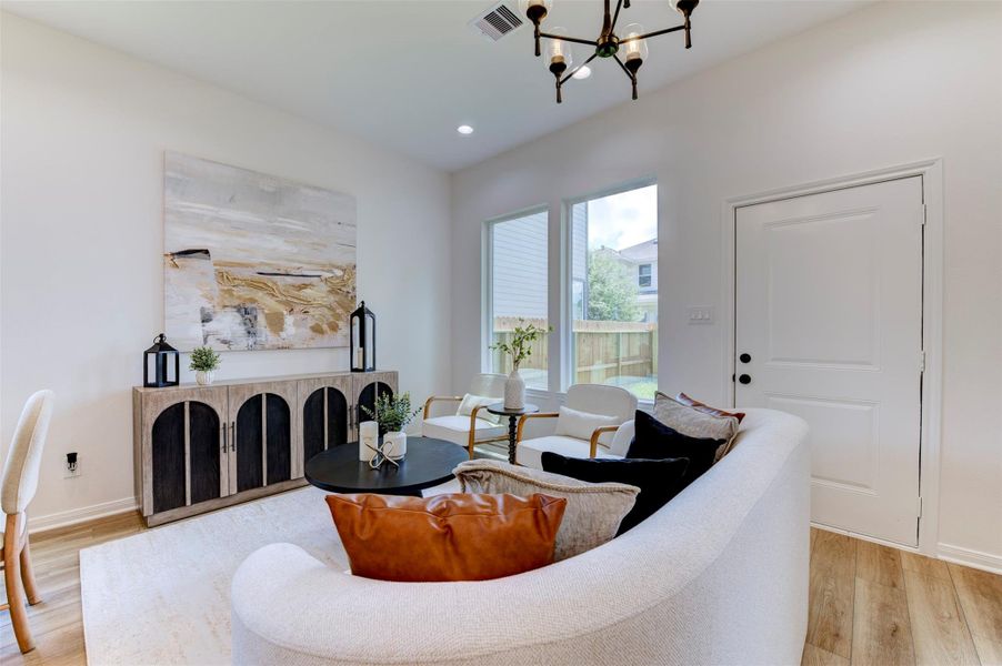 Living room detail showing hardwood floors, matte black chandelier, recessed lighting, large rear-facing windows with yard view, rear exit door, and open layout with clear sightline through the space.