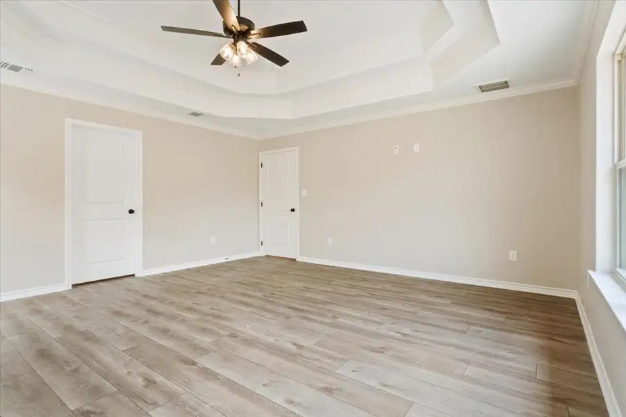 Unfurnished room featuring a tray ceiling, ornamental molding, light wood finished floors, and a ceiling fan Unfurnished room featuring a tray ceiling, ornamental molding, light wood finished floors, and a ceiling fan