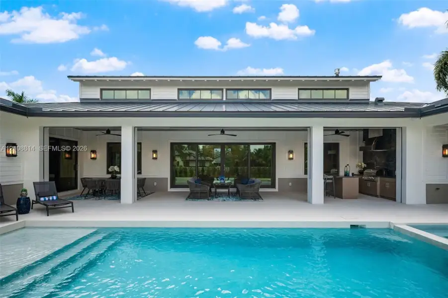 Covered lanai featuring an outdoor kitchen with built-in cabinetry, clerestory windows, metal roofing, and a swimming pool Covered lanai featuring an outdoor kitchen with built-in cabinetry, clerestory windows, metal roofing, and a swimming pool