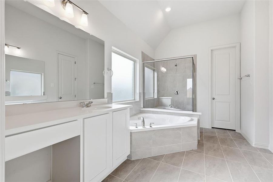 Bathroom featuring a garden tub, a stall shower, lofted ceiling, light tile patterned floors, and vanity Bathroom featuring a garden tub, a stall shower, lofted ceiling, light tile patterned floors, and vanity
