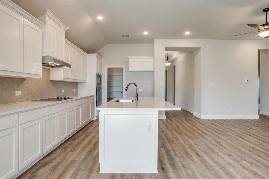 Kitchen with white cabinets, light wood-type flooring, and a kitchen island with sink