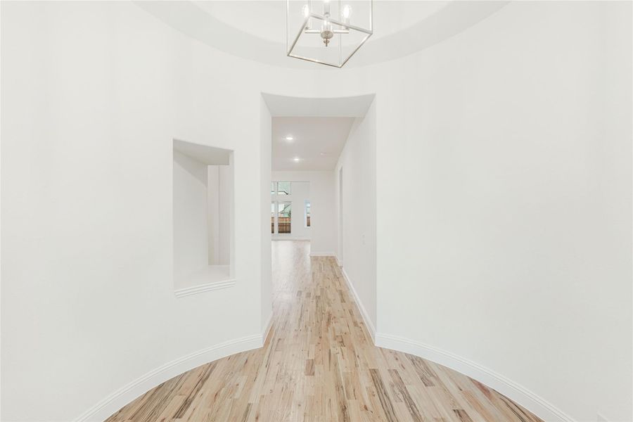 Bright entryway hallway with light wood floors, white walls, wall niche, and modern geometric chandelier overhead.