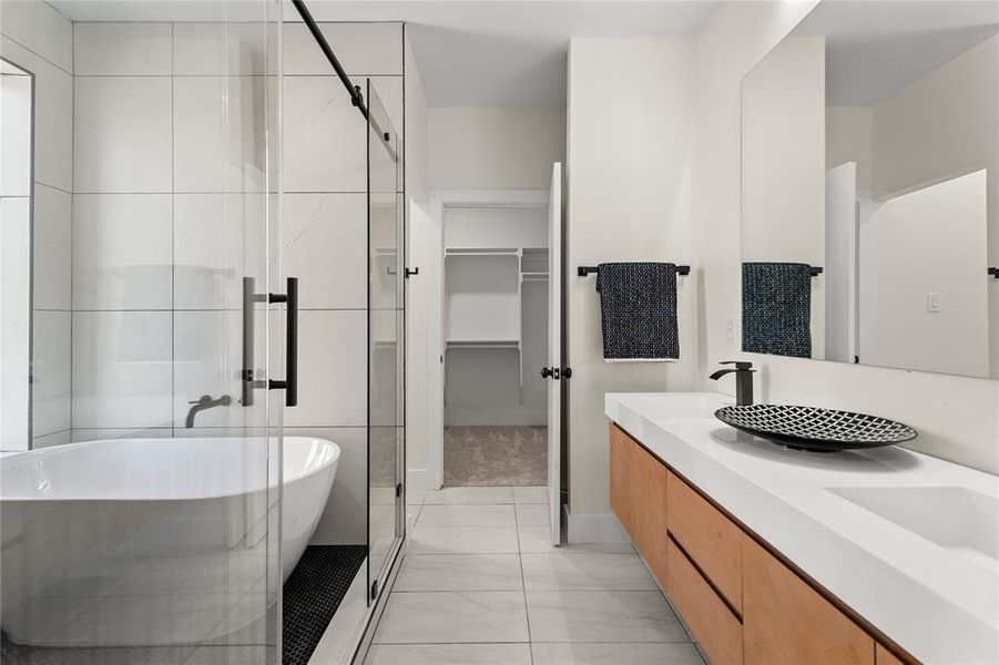 Bathroom with double vanity, a freestanding tub, a stall shower, and a walk in closet
