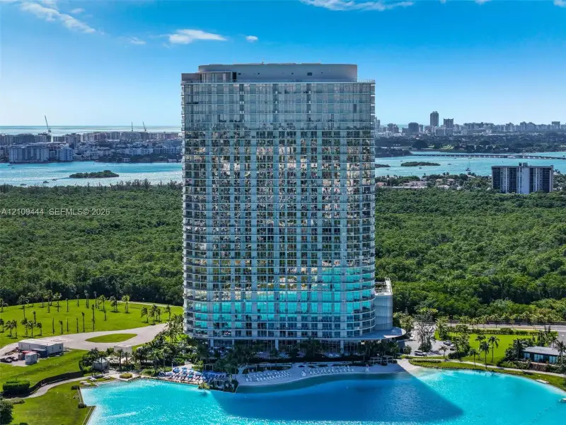 High-rise residential tower featuring a glass-curtain wall exterior, private balconies, and a multi-level structure positioned on a waterfront site with expansive green space