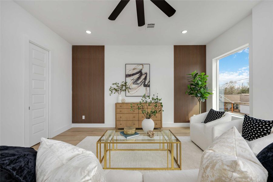 A bright, modern living room features white seating, a glass coffee table with gold accents, wood-slat accent walls, and large windows that fill the space with natural light.